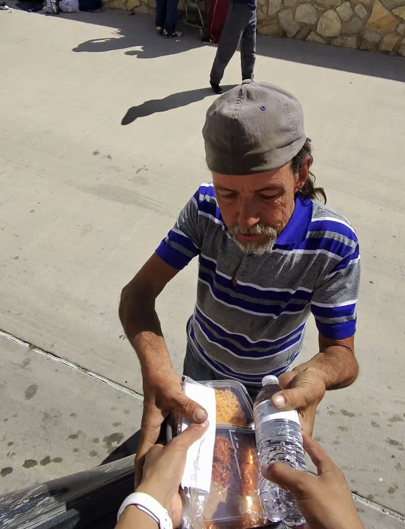 A volunteer handing a hot meal of rice and a bottle of water to a man on the street