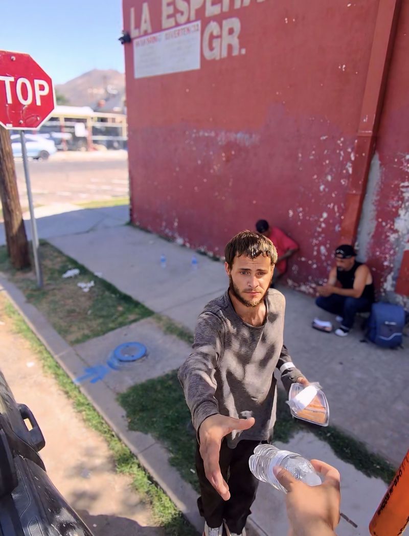 A volunteer handing water and a meal to a man in need on a street in the border region
